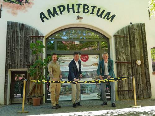 Drei Männer stehen vor einem Amphibienhaus und schneiden ein Band durch.