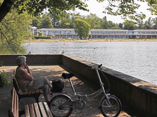 Eine ältere Dame sitzt auf einer Bank am Maschsee und schaut auf den See hinaus, neben ihr steht ein Fahrrad