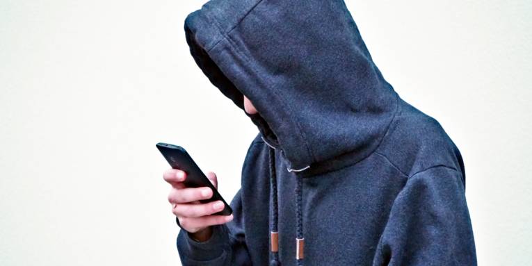 Ein Jugendlicher trägt einen Kapuzenpulli und schaut mit hängenden Schultern auf sein Smartphone.