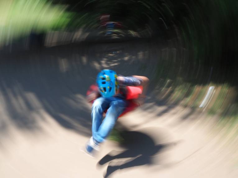 Ein Kind dreht sich mit hoher Geschwindigkeit auf einem Spielplatz-Spielgerät, Bewegungsunschärfe lässt das Bild dynamisch erscheinen.