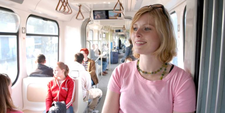 Frau mit rosa T-Shirt steht im Mittelgang einer Stadtbahn.